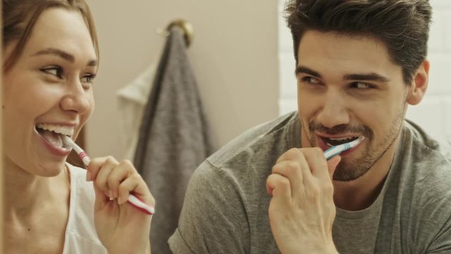 Attractive couple having fun while cleaning teeth together in bathroom with brush and toothpaste