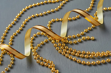 Golden ribbon and glossy long beads lies on dark scratched concrete desk. Close-up