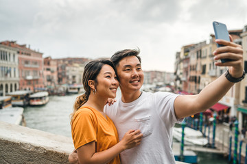 Fototapeta na wymiar Loving couple on holiday in summer in Venice, Italy - Millennials take a selfie on the famous Rialto Bridge