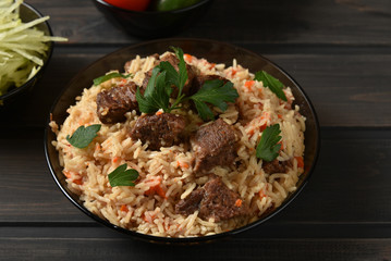 Oriental cuisine. National Uzbek pilaf with meat on a wooden table. 