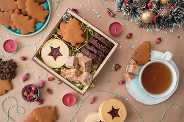 New Year and Christmas flat lay photo of a square box filled with homemade cakes. The box is on craft paper, with decorations, baking and a mug of tea around.