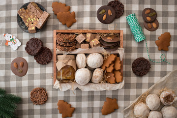 New Year and Christmas flat lay photo of rectangular wooden box filled with homemade cakes. The box is on a checkered tablecloth, with decorations and baking around.