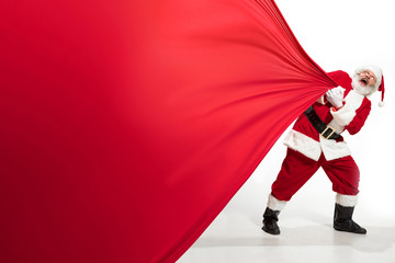 Santa Claus pulling huge bag full of christmas presents isolated on white background. Caucasian...