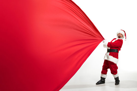 Santa Claus pulling huge bag full of christmas presents isolated on white background. Caucasian male model in traditional costume. New Year 2020, gifts, holidays, winter mood. Copyspace for your ad.