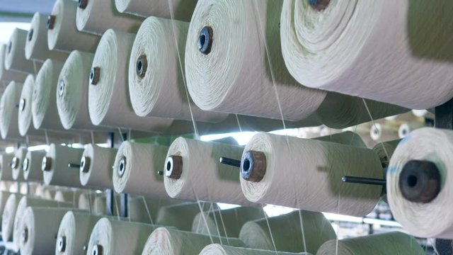 White fiber spooling on bobbins, placed on racks at a factory.