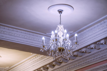 Beautiful chandelier in the old style hanging from the ceiling, its light bulbs brightly illuminate...