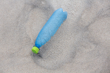 Environmental pollution - a blue plastic bottle, lying on the beach as waste