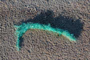 Environmental pollution - a part of an old worn plastic rope, brought back by the sea as garbage