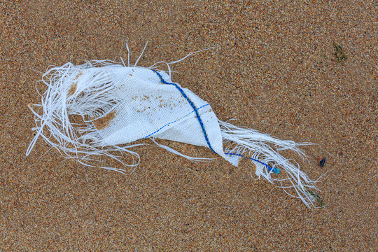Environmental Pollution - the worn-out rest of a big bag, lying on the beach as waste