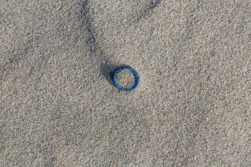 Fototapeta na wymiar Environmental pollution - a little blue hair tie, lying on the beach as waste
