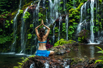 Woman sitting on the rock, practicing yoga. Young woman raising arms with namaste mudra near...