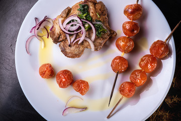 Food still life on a tray on a white plate baked meat and tomatoes on skewers decorated with red onions and olive oil