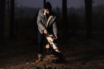 Lumberman work with a chainsaw in the forest. Strong lumberjack with the chainsow in the forest.Stylish lumberman getting ready for work. Lifestyle. Hard work in the forest. Illegal logging.