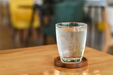 Cold water mixed with ice in a glass on wooden table.