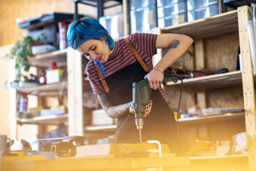 Young woman using electric drill in industrial workshop