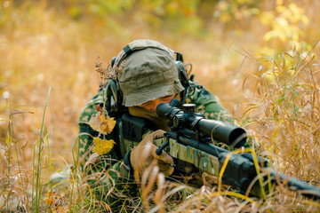 Airsoft man in uniform lay in grass with sniper rifle. Soldier aims at the sight