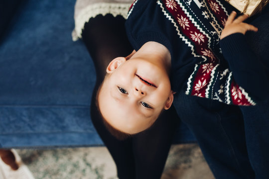 Low Perspective Portrait Of Cute Little Boy Smiling At Camera Wearing Red Santa Hat And Warm Sweater With Snowflakes.