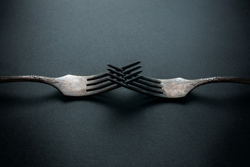 two elegant old vintage forks coupled together on a black background close-up. competition concept.