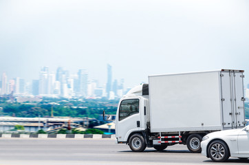 A small white truck running on the road for a transportation business with a city background.