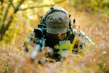 Closeup man in uniform with sniper rifle, front view. Airsoft soldier lay in long grass and check...
