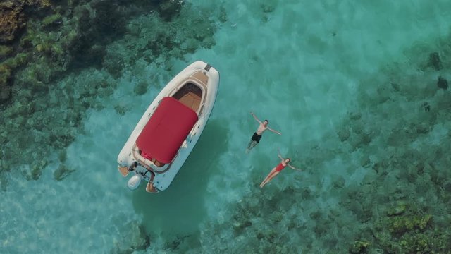 Aerial view of a couple lying on a crystal clear water near a boat. They have the best vacation ever on a hot sunny day. Beautiful nature. 