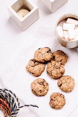 Christmas cranberry and chocolate oatmeal cookies and mug of cocoa with marshmallow on white background decorated candles. Selective focus