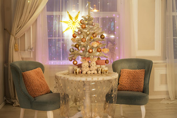 A beautiful room decorated for Christmas: a table with an openwork tablecloth, a small New Year tree with garlands, two velvet chairs with pillows and a luminous star on the window.