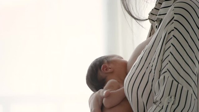 Close up shot of mother give breastfeeding newborn baby in front of glass window with white curtain and also slow motion movement.