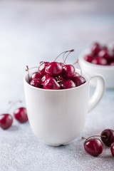 Fresh cherry in white mug on gray stone background Close-up