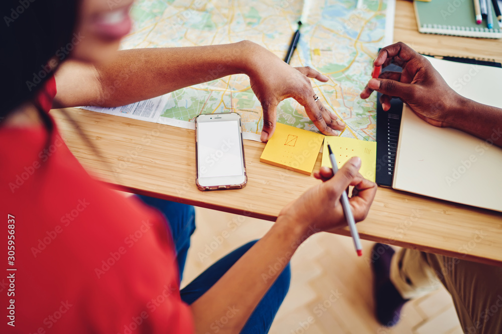 Poster cropped image of male and female planning adventure journey at table making notes on yellow stickers