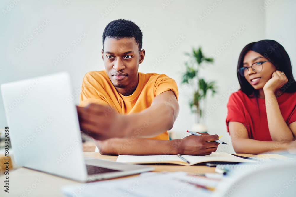 Poster serious african american hipster guy pointing on laptop computer browse information for doing homewo
