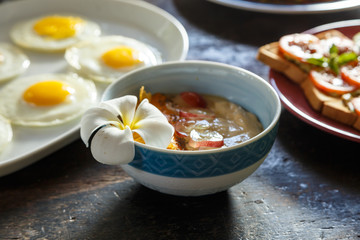 wooden table is covered with healthy variety of natural food, banana porridge, scrambled eggs, omelet with vegetables