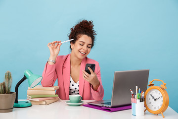 Image of laughing brunette woman using cellphone while working at desk