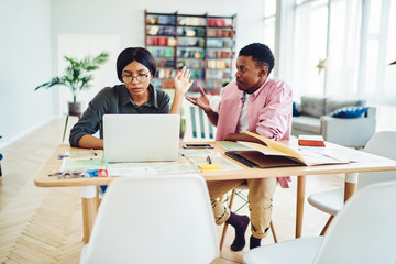 Serious male and female students having discussion and disagreements during working process at bright room, african american woman gesture ignore man's explanation looking at laptop computer.