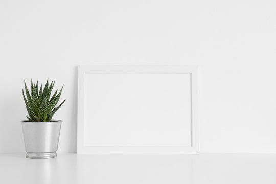 White frame mockup with a cactus in a pot on a white table.Landscape orientation.