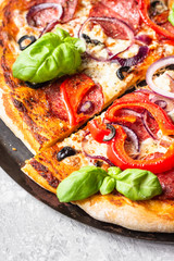 Tasty pizza with salami, onion, pepper, olives, mozzarella cheese and basil on black tray. Homemade hot pepperoni pizza.