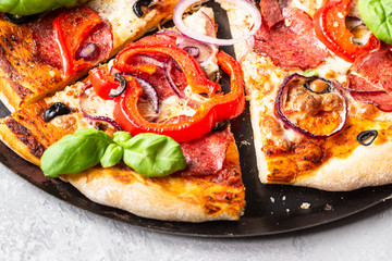 Tasty pizza with salami, onion, pepper, olives, mozzarella cheese and basil on black tray. Homemade hot pepperoni pizza.