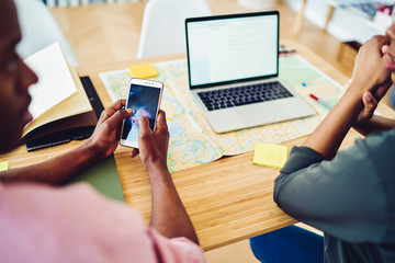 Cropped image of african american male holding modern smartphone connecting to laptop computer for...