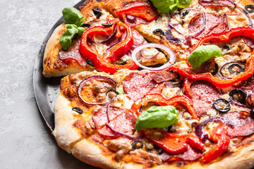 Tasty pizza with salami, onion, pepper, olives, mozzarella cheese and basil on black tray. Homemade hot pepperoni pizza.