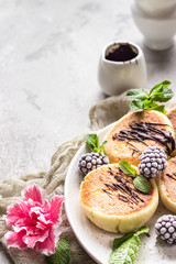 Cottage cheese pancakes or curd fritters with blackberries, melted chocolate and mint on ceramic plate. Traditional Ukrainian and Russian syrniki. Gourmet Breakfast.