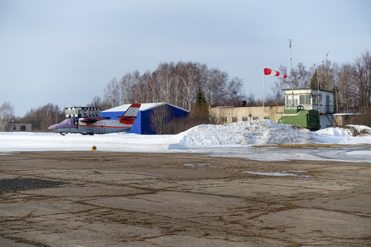 The airplane, covered with a cloth cover, stands on a snowy old airfield of local air lines, against the background of a control tower.