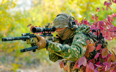 Closeup man in green uniform with sniper rifle. Airsoft soldier stand in bush and aims at the sight