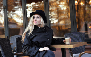 Young beautiful woman in hat sitting in a cafe and drinking a cappuccino.