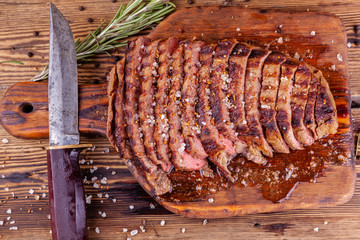 Chopped Grilled Steak Rib Eye on Rustic Cutting Board with Vintage Knife on Wooden Background. Juicy Medium Ribeye Steak with Salt, Pepper and Rosemary. Concept of Delicious Meat Food. Top View