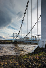 Small cable bridge empty road, suspension bridge crossing river, dramatic sky by the sunset