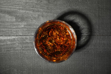 Glass of whiskey with ice cubes on dark wooden background, top view