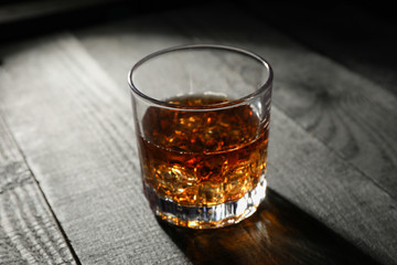 Glass of whiskey with ice cubes on dark wooden background, space for text