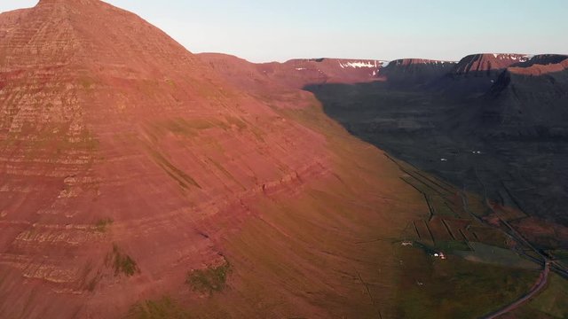 High aerial flight over a mountain lit by bright midnight sun in westfjord Iceland