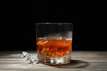 Glass of whiskey with ice cubes on wooden background, space for text
