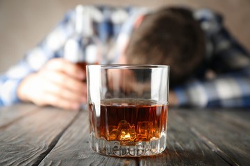 Glass of whiskey against drunk man on wooden background, close up